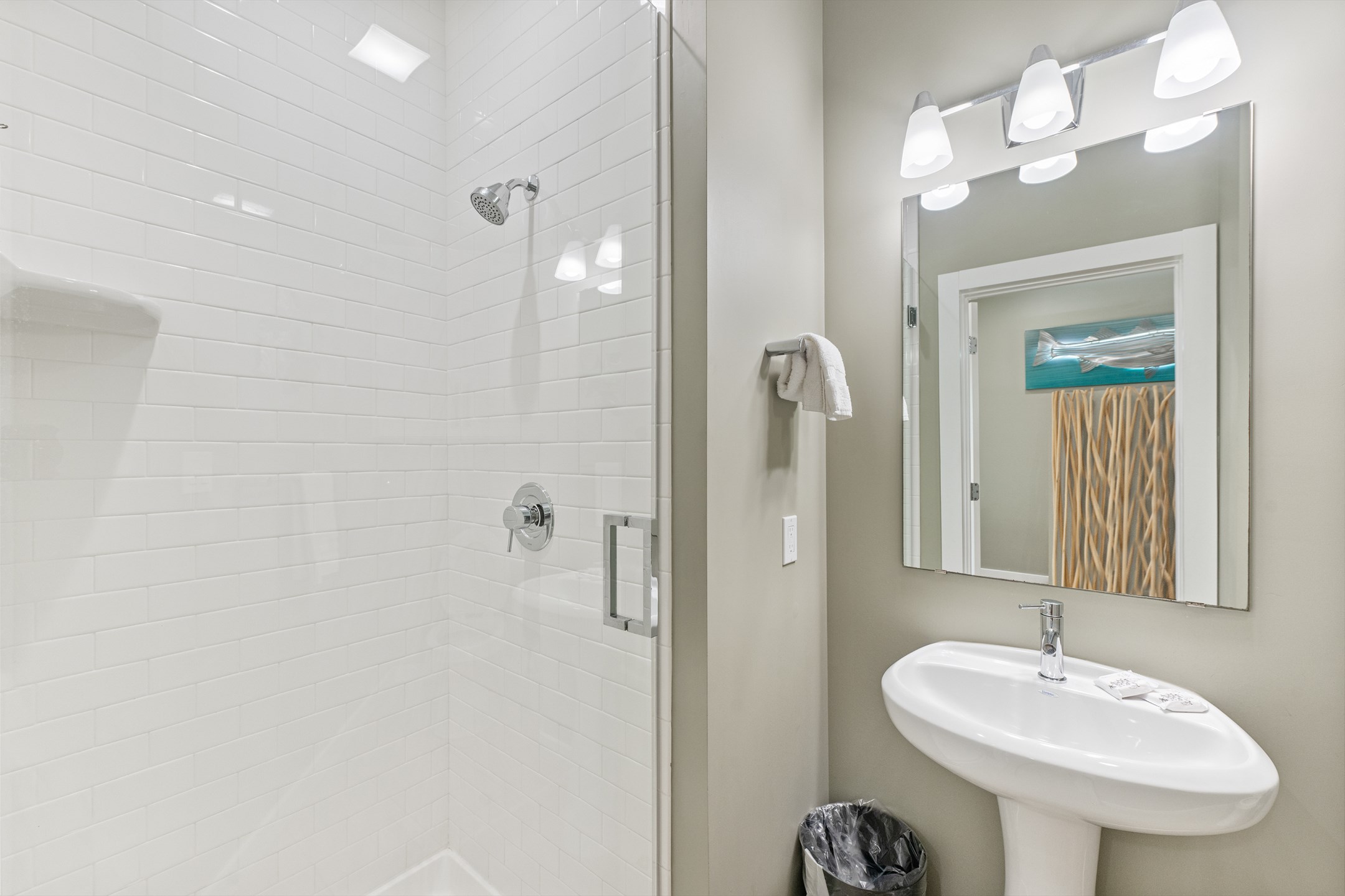 Downstairs bathroom features a walk-in shower and pedestal sink, offering a spacious, beachy retreat for everyone to get ready