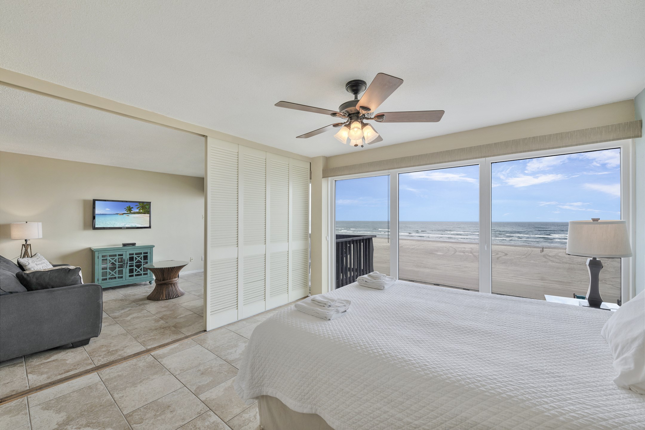 Primary bedroom with queen size bed, private bathroom and floor to ceiling windows offering a view of the beach - shutters that open up into the living area