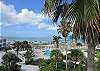 Stunning view of the Gulf of Mexico and pool area from a beach house rental, surrounded by lush palm trees and pristine sandy beaches.