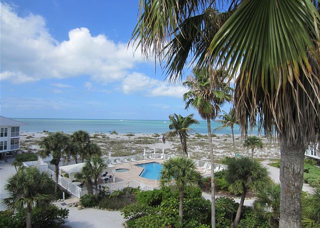 Stunning view of the Gulf of Mexico and pool area from a beach house rental, surrounded by lush palm trees and pristine sandy beaches.