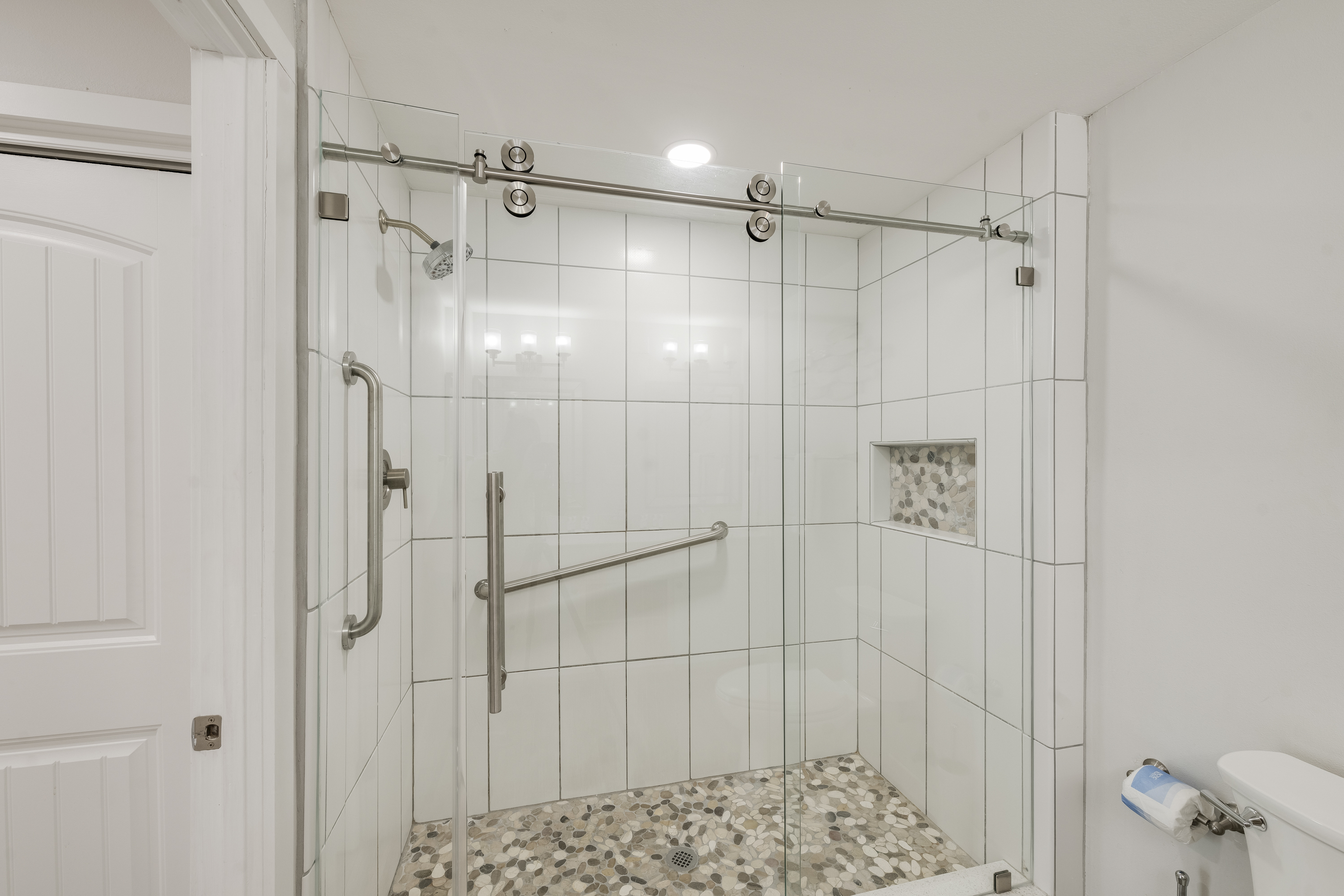 modern walk-in shower with a frameless glass sliding door and a horizontal grab bar that adds accessibility and safety.