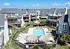 Inviting community pool with clear blue water, surrounded by comfy loungers and straw covered structures.