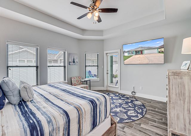 The primary bedroom features a king-size bed, a mounted TV and an armoire for extra storage