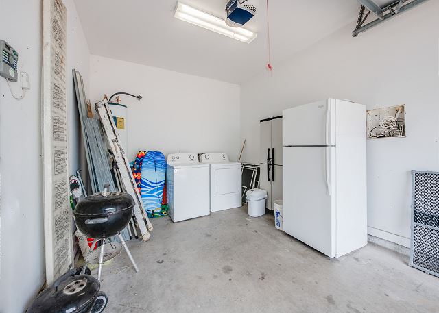 Laundry station in garage with spare refrigerator, BBQ, and beach accessories  