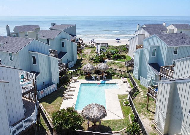 Inviting community pool with clear blue water, surrounded by comfy loungers and straw covered structures.