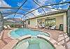Screened in pool area with lounge chairs and covered seating area with TV and BBQ
