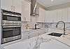 The chef’s kitchen features white shaker cabinetry, Quartz countertops, a large waterfall island with seating for four, double wall ovens, stainless appliances and a coffee bar. 