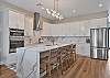 The chef’s kitchen features white shaker cabinetry, Quartz countertops, a large waterfall island with seating for four, double wall ovens, stainless appliances and a coffee bar. 