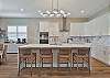 The chef’s kitchen features white shaker cabinetry, Quartz countertops, a large waterfall island with seating for four, double wall ovens, stainless appliances and a coffee bar. 