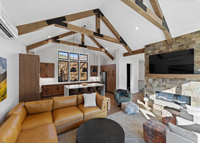 The open concept living area offers ample seating, air conditioning, cozy fireplace, a mounted TV, and a vaulted ceiling. 