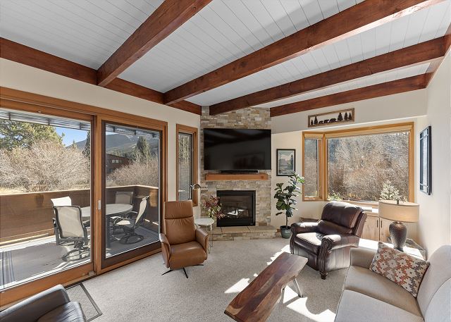 Living area with a mounted TV over a gas fireplace, ample seating, and deck access. 