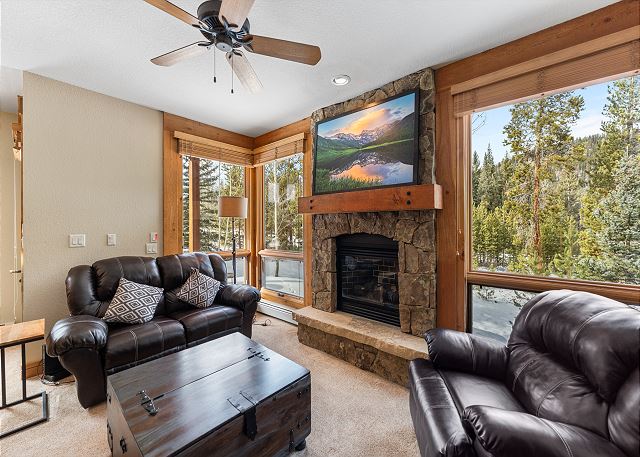 Living area with cozy seating surrounding a fireplace and mounted TV. 