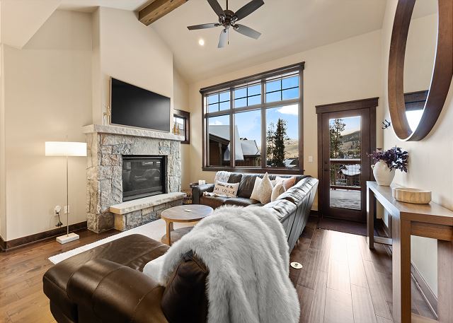 Living area with a cozy stone surround fireplace, mounted TV, and balcony access. 
