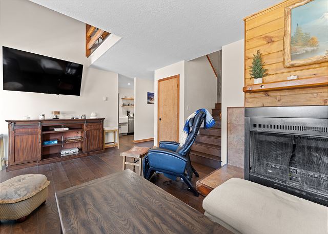Living room with a wood-burning fireplace, mounted smart TV, massage chair, and Bluetooth speaker. 