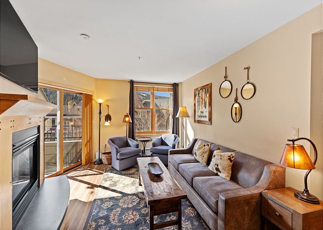 Living area with mounted flat screen TV, gas fireplace, balcony access, hardwood flooring and sleeper sofa. 