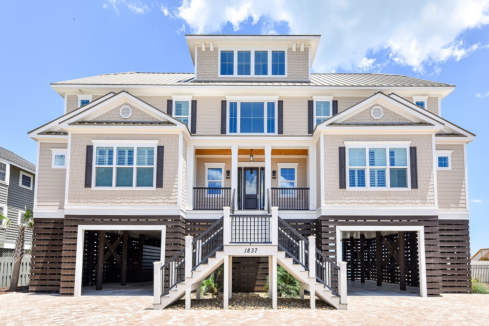 A two story home with stairs leading down to the beach.