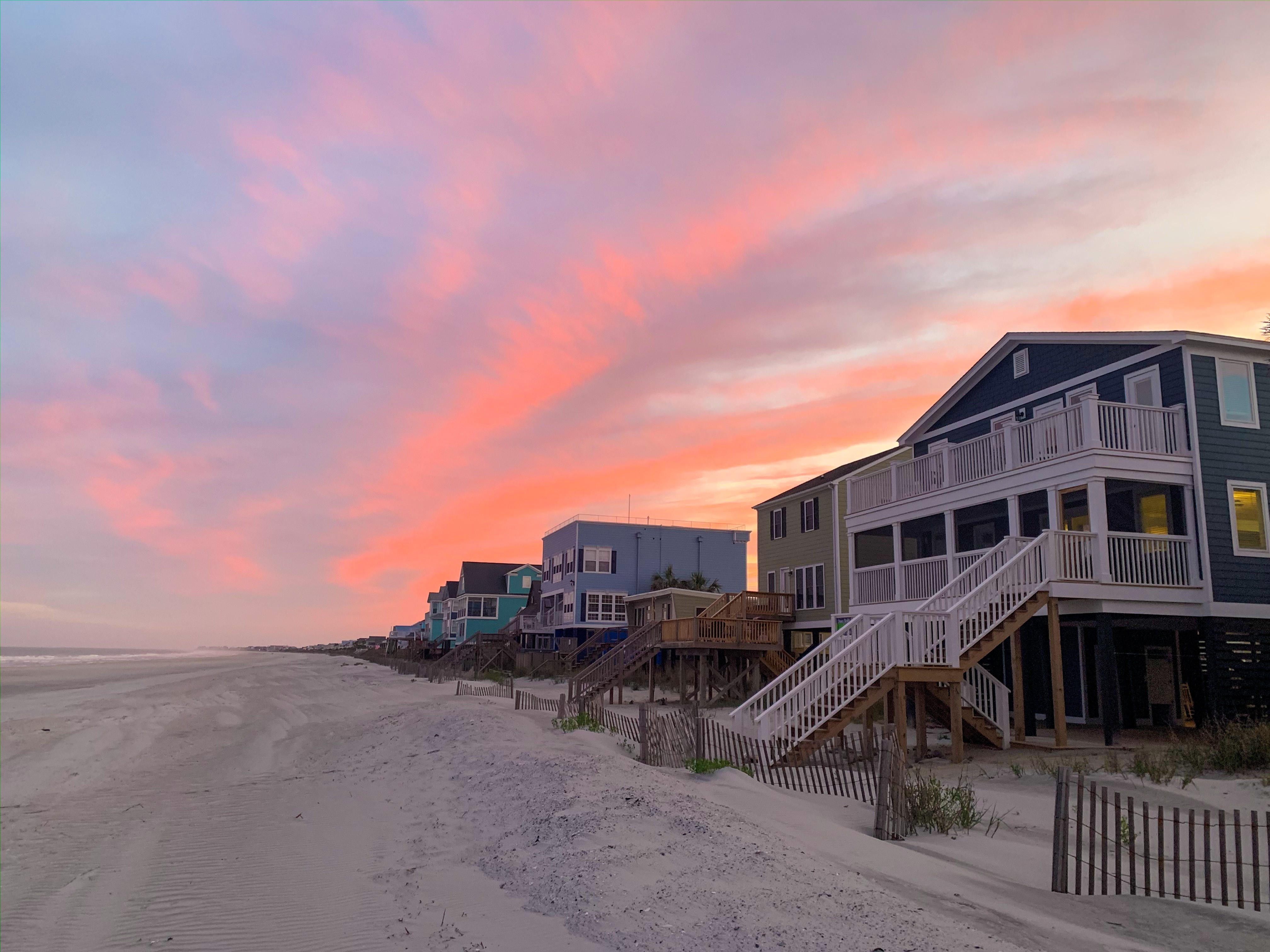 Photo of the South Myrtle Beach with rows of beach houses on the right side. The sky is early morning pink. 