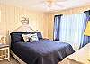 Spacious master bedroom at D4 Briar Court featuring navy coastal bedding, a white headboard, and soft yellow paneled walls.