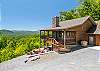 Side view from the driveway showing the covered deck, fire pit, and mountain views behind the cabin.