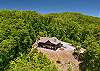 Close aerial view of the cabin's roofline, deck, chimney, and fire pit.