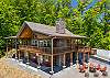 Side and front cabin view showing the two-level deck, stone chimney, and fire pit area.