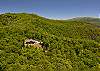 High aerial view of the cabin on a cleared mountain lot surrounded by forest.