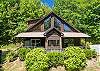 Straight-on shot of the cabin's A-frame gable, expansive windows, and deck with a hot tub. 